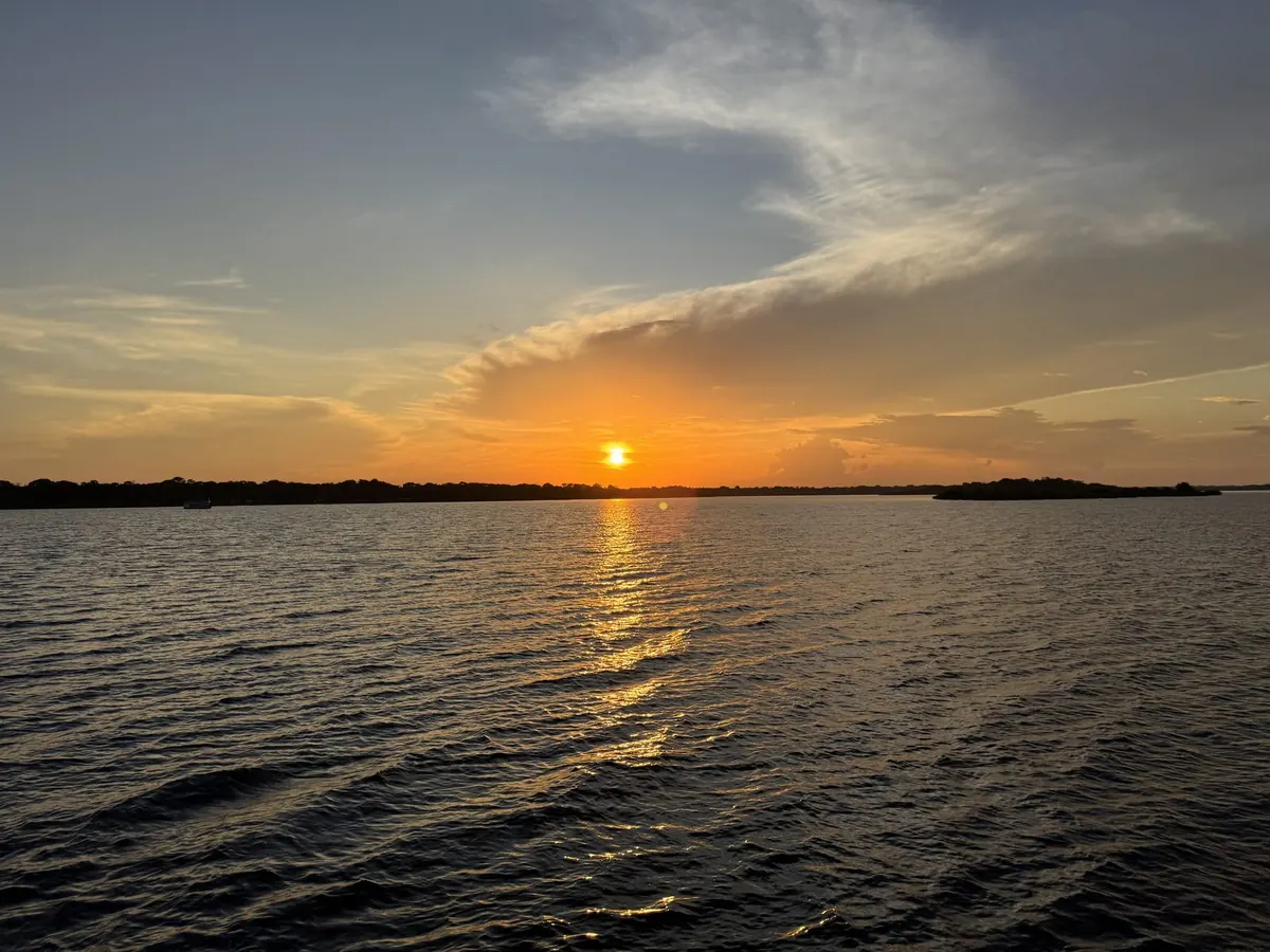 Sunset over the Rio Negro, the sun dropping behind the forest line and its light stretching across the water