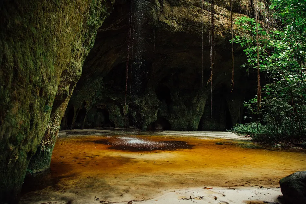 Amber-tinted pool inside a sandstone cave with a waterfall curtain, Gruta da Judeia, Presidente Figueiredo
